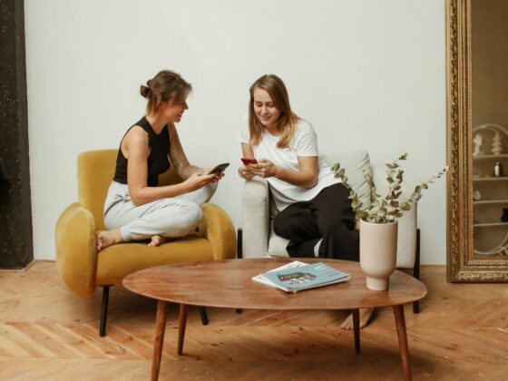 Dvije prijateljice sjede u dnevnoj sobi, smiju se i gledaju u mobitel.