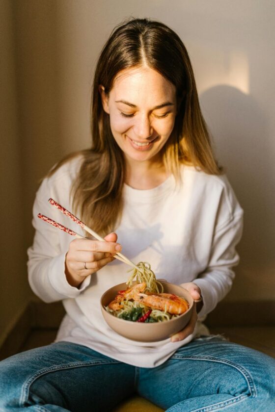 Žena uživa u zdjeli rezanaca i prakticira mindful eating, fokusirana na obrok bez distrakcija.