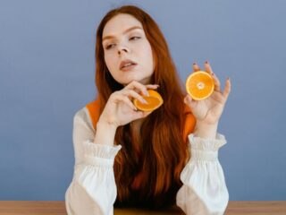 Žena sjedi za stolom i drži polovice naranče, ilustracija istraživanja o povezanosti prehrane, mikrobioma i mentalnog zdravlja