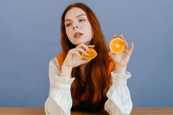 Žena sjedi za stolom i drži polovice naranče, ilustracija istraživanja o povezanosti prehrane, mikrobioma i mentalnog zdravlja