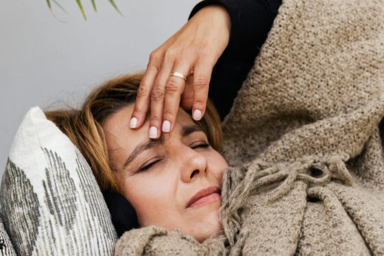 Žena s migrenom leži na kauču i drži ruku na čelu, ilustracija kako su migrena i stres povezani u svakodnevnom životu